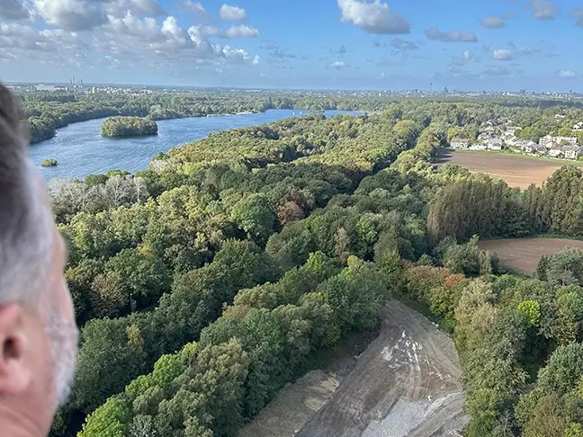 Mann blickt von oben auf einen weitläufigen Wald und einen See, dahinter ist eine Stadt zu erkennen.